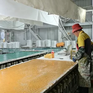 FRP grating manufacturing: Two workers use tools to process fiberglass strands and resin on a large mold table, producing composite grating panels.