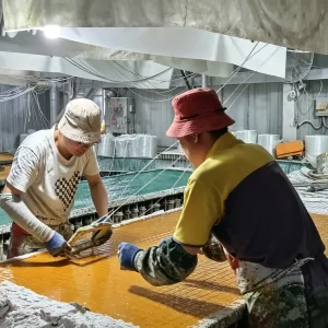 FRP grating factory overview: Multiple mold stations in different stages of production (yellow and green resin) line the workshop floor, with workers processing composite panels.