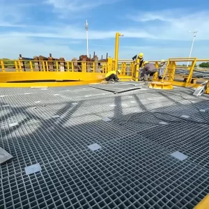 Industrial workers installing gray molded FRP grating on a yellow safety railing platform, corrosion-resistant fiberglass walkway grating for industrial use